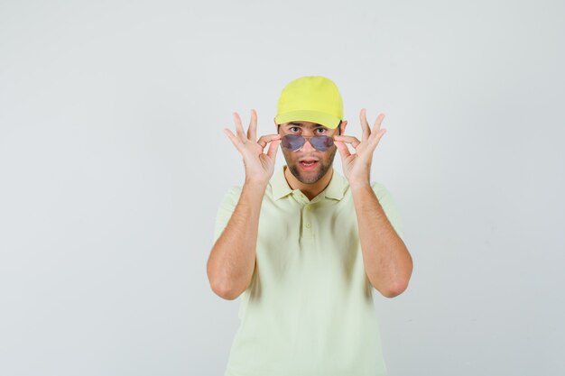 Uomo di consegna che toglie gli occhiali in uniforme gialla e sembra sospettoso, vista frontale.