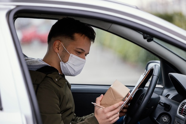 Uomo di consegna vista laterale con maschera in auto