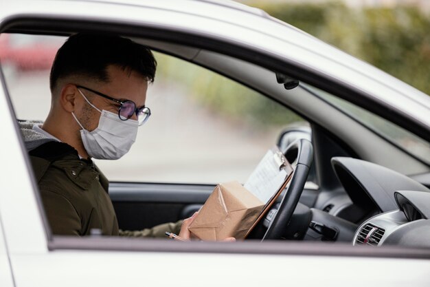 Uomo di consegna vista laterale con maschera in auto