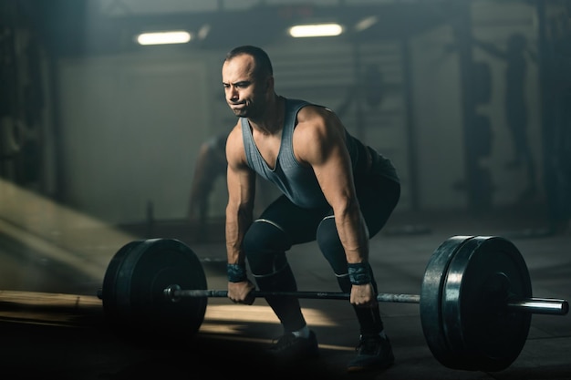 Uomo di corporatura muscolare che fa uno sforzo durante il sollevamento pesi durante l'allenamento incrociato in palestra