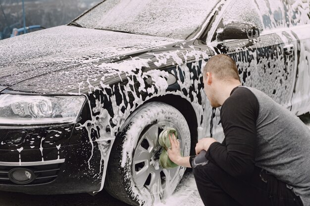 Uomo di Handsomen in un maglione nero che lava la sua automobile