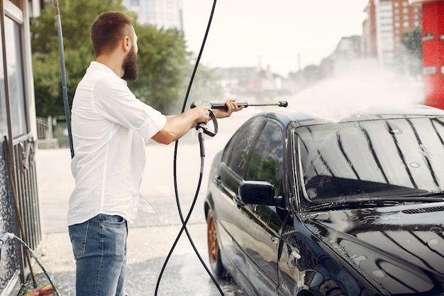 Uomo di Handsomen in una camicia bianca che lava la sua automobile