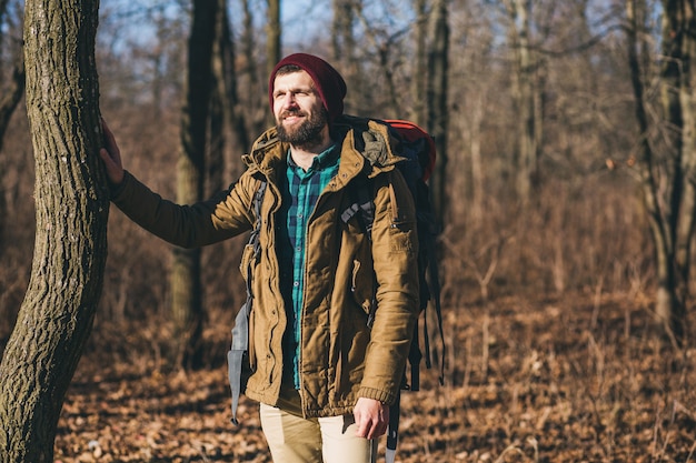 Uomo di hipster che viaggia con lo zaino nella foresta di autunno che indossa giacca calda, cappello, turista attivo, esplorando la natura nella stagione fredda