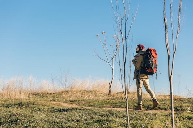 Uomo di hipster che viaggia con lo zaino nella foresta di autunno che indossa giacca calda, cappello, turista attivo, esplorando la natura nella stagione fredda