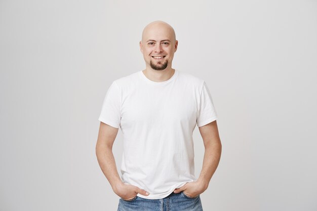 Uomo di mezza età calvo sorridente bello con la barba che indossa la maglietta bianca casuale