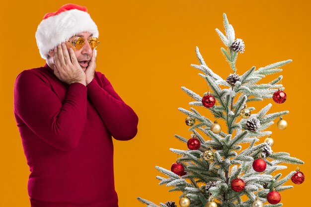 Uomo di mezza età che indossa il cappello di Babbo Natale in dolcevita rosso scuro e occhiali gialli