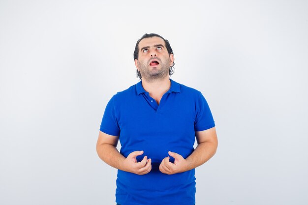 Uomo di mezza età che tiene le mani in modo aggressivo in t-shirt polo e sembra annoiato. vista frontale.