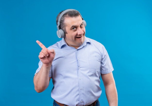 Uomo di mezza età in cuffie con emozione sorpresa sul viso che punta il dito indice su uno sfondo blu