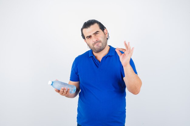 Uomo di mezza età in t-shirt polo che tiene una bottiglia d'acqua mentre mostra il gesto giusto e sembra esitante, vista frontale.