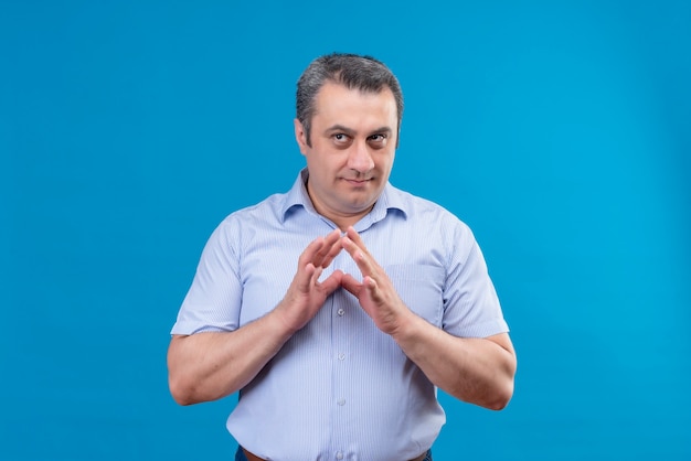 Uomo di mezza età pensante e confuso in camicia spogliata blu che tiene le mani insieme su una priorità bassa blu