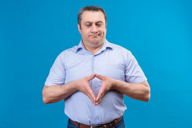 Uomo di mezza età scontento e confuso in camicia a righe blu pensando e tenendosi per mano insieme su uno spazio blu