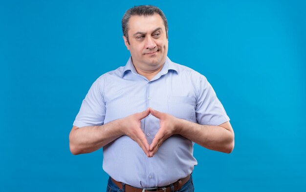 Uomo di mezza età serio e arrabbiato in camicia a righe verticali blu che osserva rigorosamente tenendo le mani insieme su una priorità bassa blu