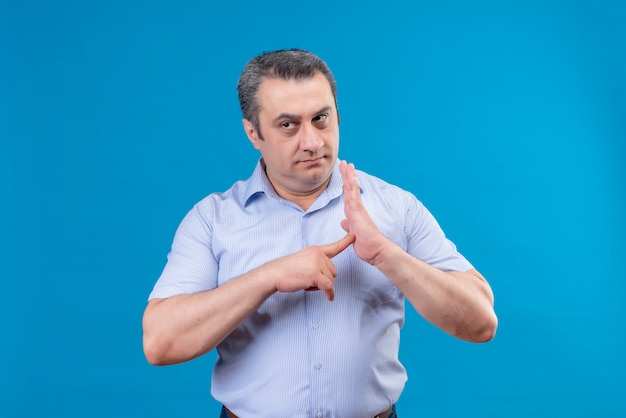 Uomo di mezza età serio e rigoroso in camicia a righe blu che punta con il dito indice al centro del palmo su sfondo blu