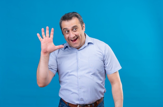 Uomo di mezza età sorridente e positivo in camicia blu che dà il gesto cinque su una priorità bassa blu