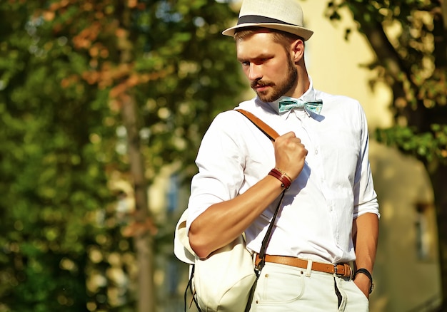 Uomo di modello bello hipster in abiti estivi alla moda in posa in cappello con borsa