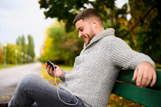 Uomo di smiley con smartphone e auricolari su una panchina