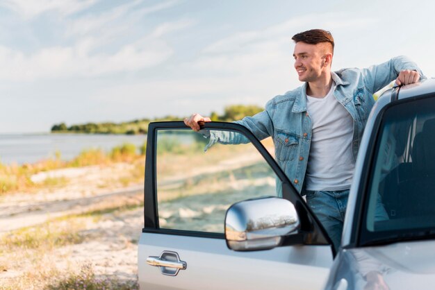 Uomo di smiley del colpo medio che posa con l'auto