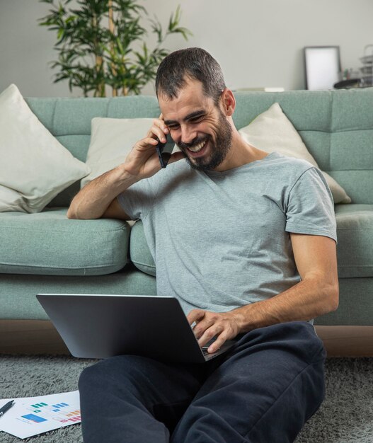 Uomo di smiley parlando al telefono a casa mentre si lavora al computer portatile