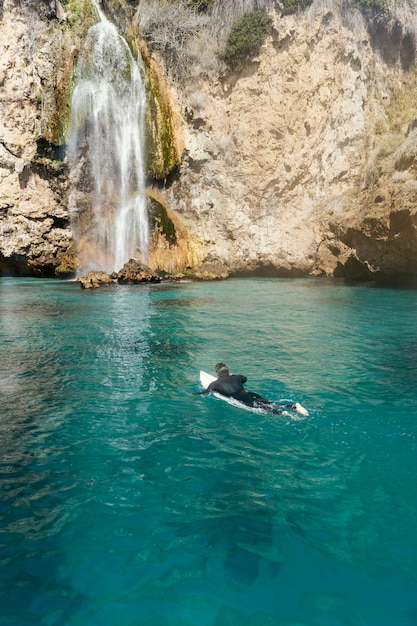 Uomo di tiro lungo che nuota con la tavola da surf