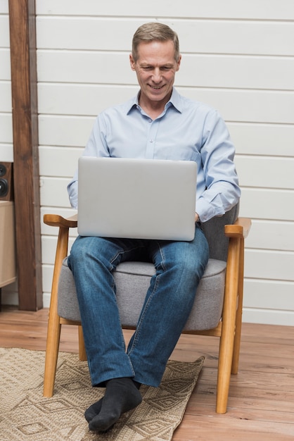 Uomo di vista frontale che si siede su una sedia mentre guardando su un computer portatile