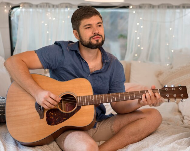 Uomo di vista frontale che suona la chitarra in una roulotte