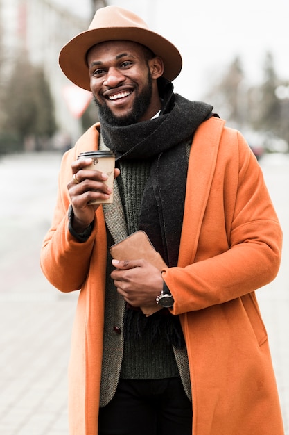 Uomo di vista frontale in cappotto arancio che tiene una tazza di caffè fuori