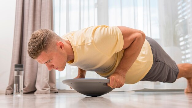 Uomo di vista laterale che lavora a casa utilizzando la palla bosu