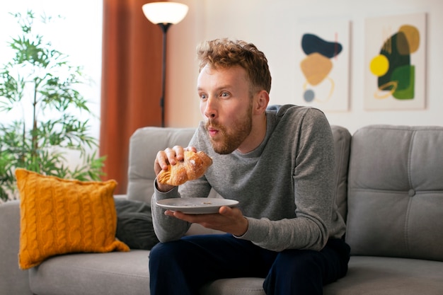 Uomo di vista laterale che mangia croissant