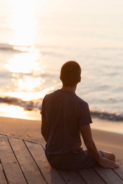 Uomo di vista posteriore meditando sulla spiaggia