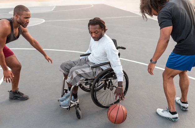 Uomo disabile in sedia a rotelle che gioca a basket con i suoi amici