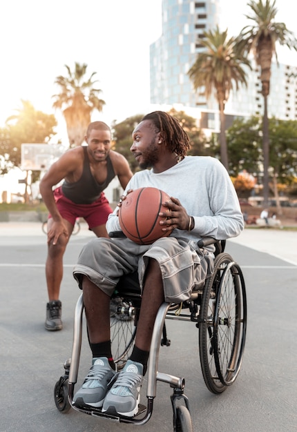 Uomo disabile in sedia a rotelle che gioca a basket con i suoi amici