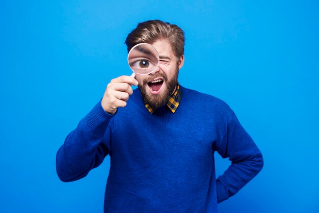 Uomo divertente che guarda il suo bulbo oculare nella lente d'ingrandimento