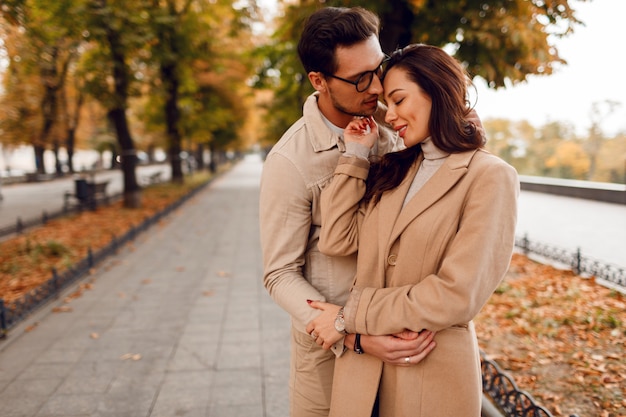 Uomo e donna alla moda imbarazzanti mentre si frequentano nel parco di autunno. Indossa eleganti cappotti beige. Umore romantico.