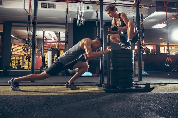 Uomo e donna atletici con manubri che si allenano e che si esercitano in palestra.