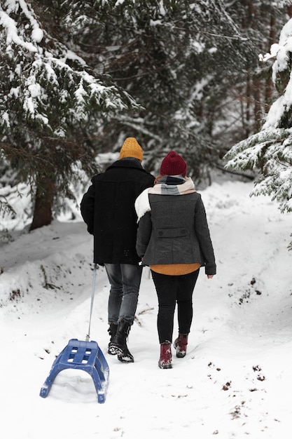 Uomo e donna che camminano nella foresta con la slitta da dietro il colpo