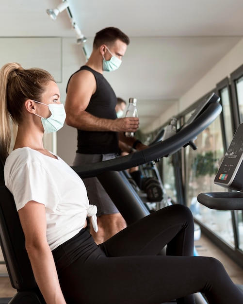 Uomo e donna che lavorano in palestra con maschere mediche