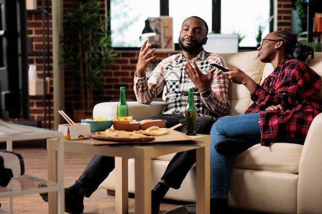 Uomo e donna che si godono la consegna di fast food e guardano la tv, cambiando canale per trovare film in televisione. Mangiare un pacchetto di pasti da asporto e bere birra dalla bottiglia, attività per il tempo libero.