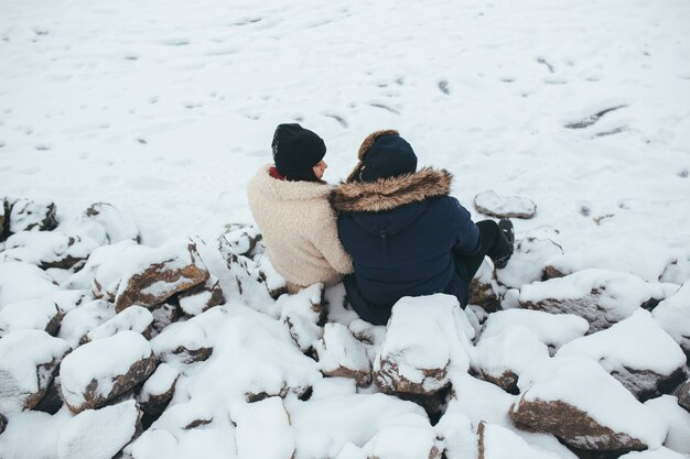 Uomo e donna che si siedono sulle rocce coperte di neve, sulla riva del lago