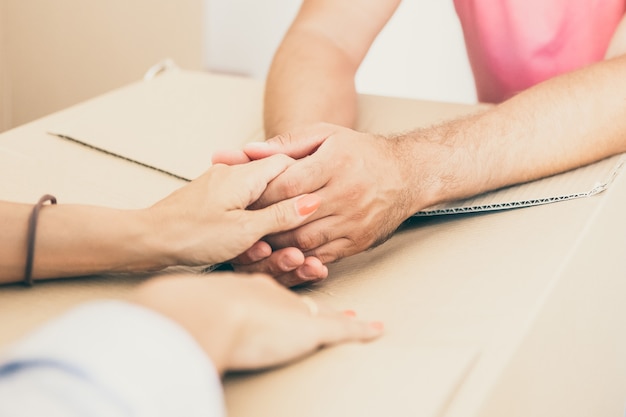 Uomo e donna che si sostengono a vicenda e si tengono per mano su un pacco di cartone, mentre si trasferiscono nel nuovo appartamento.