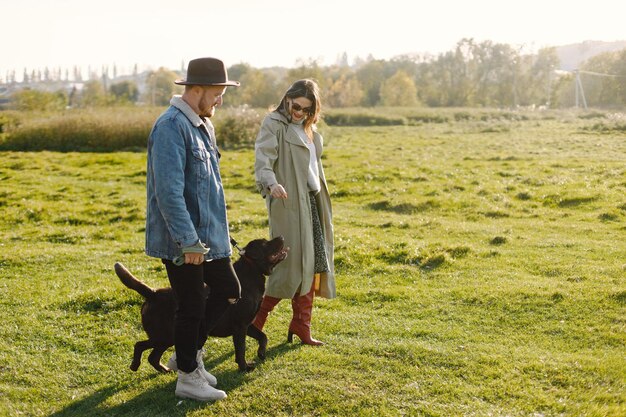 Uomo e donna in abiti alla moda che riposano su una natura con il loro labrador. Uomo che indossa una giacca e un cappello nero e una gonna da donna e stivali rossi