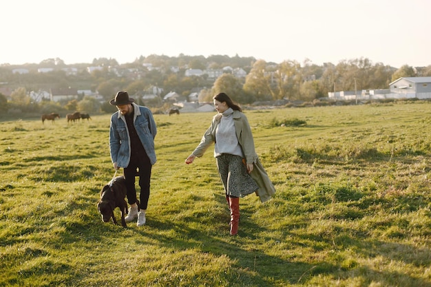 Uomo e donna in abiti alla moda che riposano su una natura con il loro labrador. Uomo che indossa una giacca e un cappello nero e una gonna da donna e stivali rossi