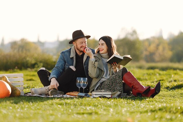 Uomo e donna in abiti alla moda seduti su una natura su un tappeto da picnic. Uomo che indossa una giacca e un cappello nero e una gonna da donna e stivali rossi