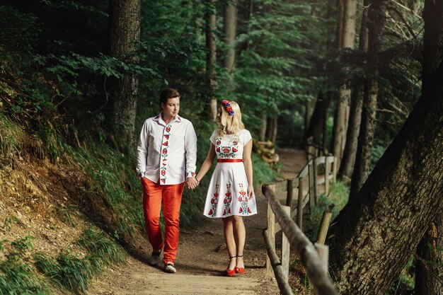 Uomo e donna in abiti ricamati camminano lungo il sentiero di legno nella foresta