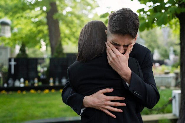 Uomo e donna in lacrime abbracciati al cimitero