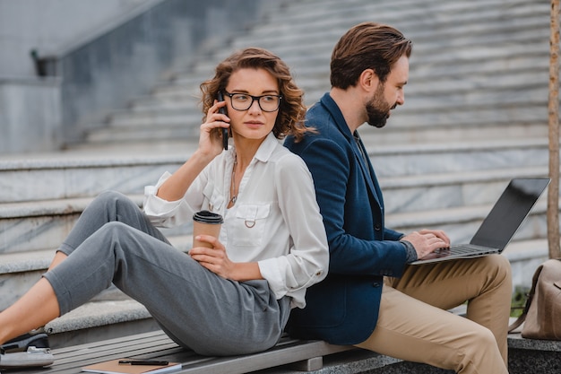 Uomo e donna sorridenti attraenti che parlano al telefono seduti sulle scale nel centro urbano della città