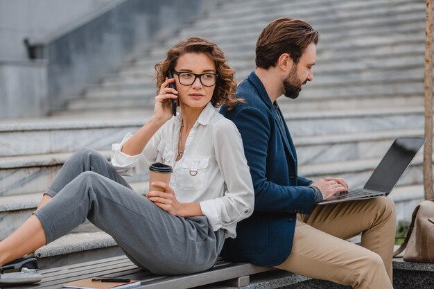 Uomo e donna sorridenti attraenti che parlano al telefono seduti sulle scale nel centro urbano della città