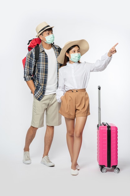 Uomo e donna vestiti per viaggiare, che indossano maschere insieme ai bagagli
