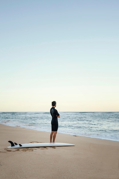 Uomo e tavola da surf al colpo lungo dell'oceano