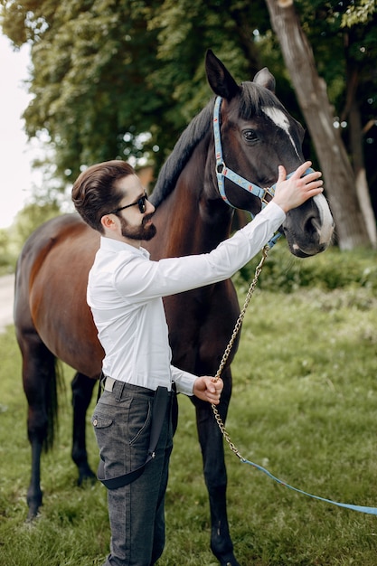 Uomo elegante che sta accanto al cavallo in un ranch