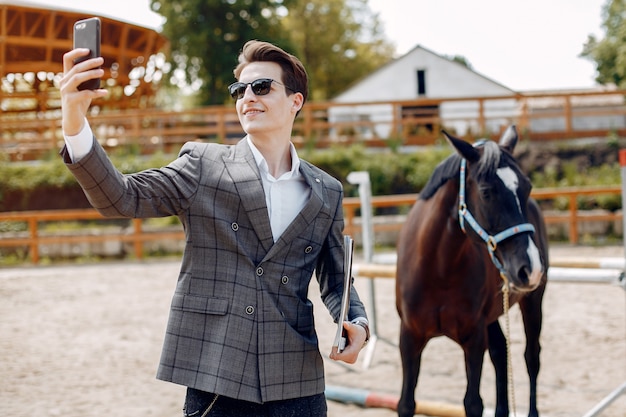 Uomo elegante che sta accanto al cavallo in un ranch